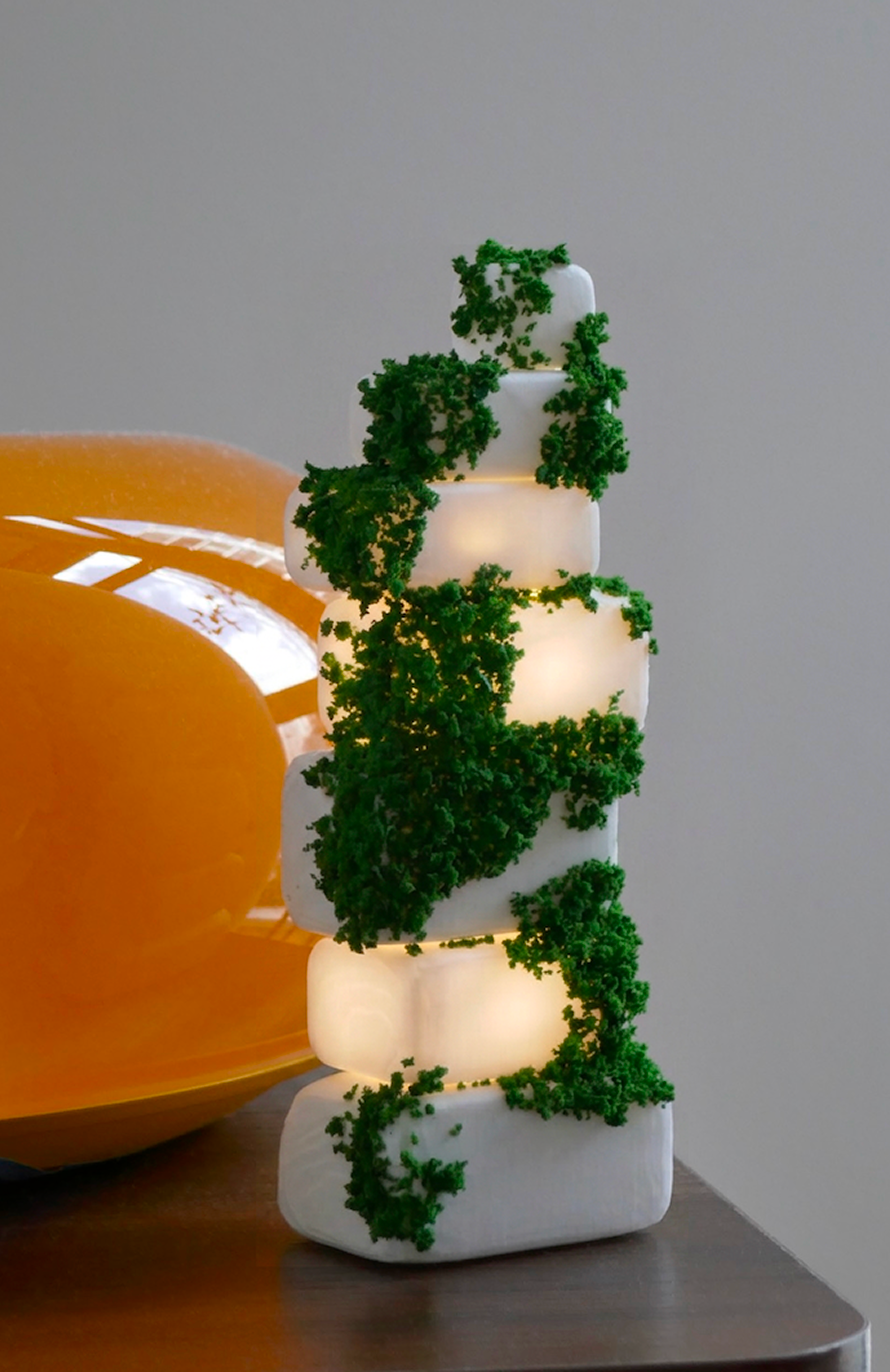 Cairn in its ON state — warm light glowing from between the stacked 3D-printed stones, moss threading up the form